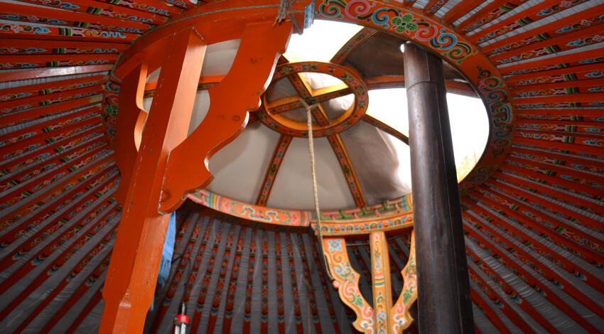 Interior ceiling of a Mongolian ger with a toono crown window at the center, two support pillars, and radiating roof poles.