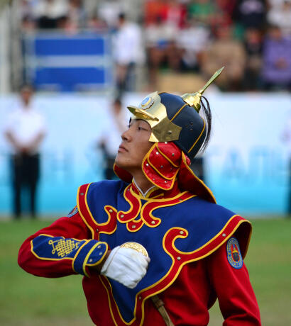 Honor guard in ceremonial red and blue uniform, plumed helmet with gold decorations
                            at Mongolian Naadam festival.