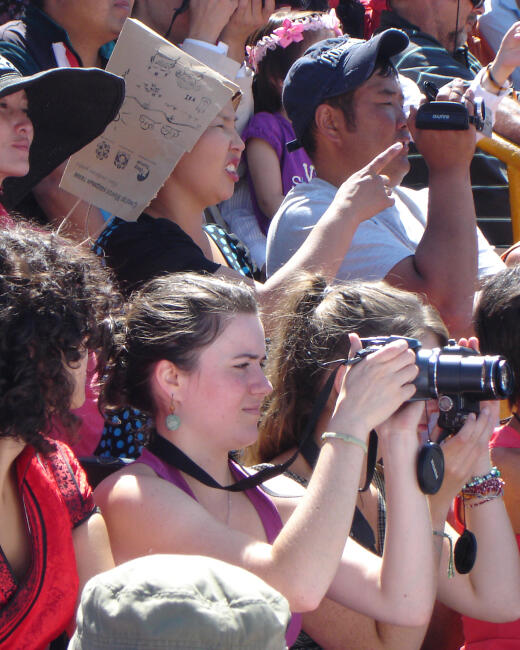 A tourist taking photos with a camera in a crowd of spectators at Mongolia's Three Manly Games festival stadium.