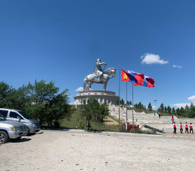 Chinggis Khaan's silver equestrian statue towering over its complex, with Mongolian flags and tourists below.