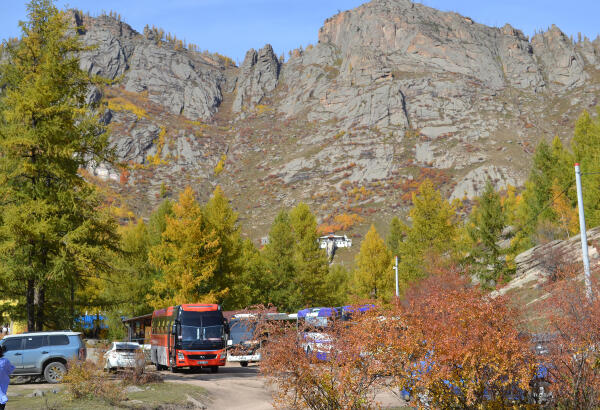 Tourist buses and autumn trees at the foot of the Ariyabal Buddhist meditation temple, perched on a mountainside.