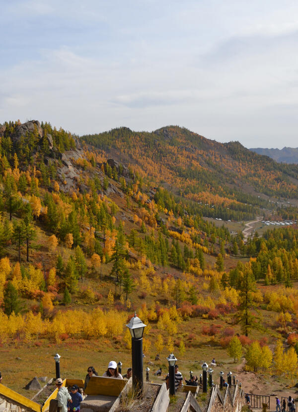 Autumn landscape of Terelj National Park viewed from Ariyabal Temple, with golden trees, hills, and visitors.